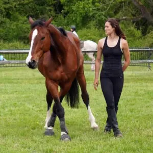 A woman walking with her horse in the grass.