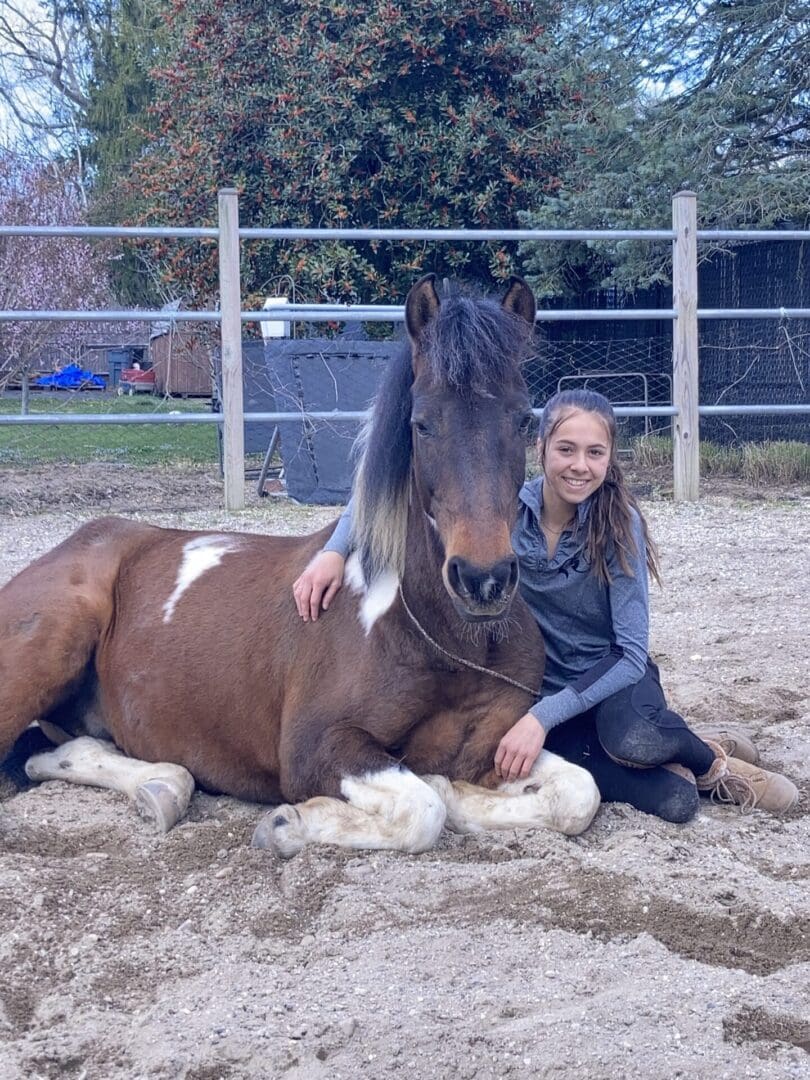 A girl sitting on the ground next to a horse.